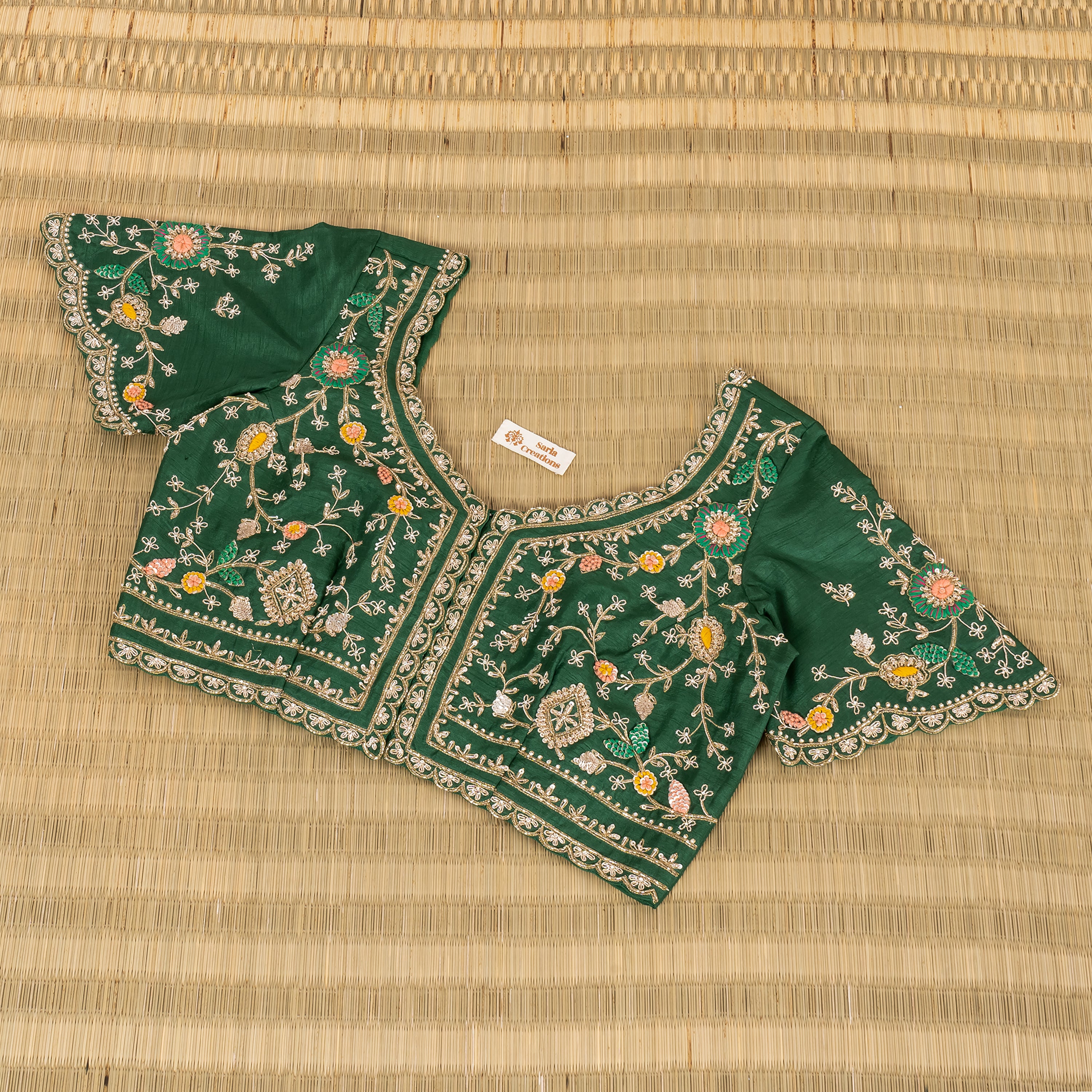 A dark green embroidered blouse top with floral and geometric patterns, laid flat on a woven straw mat background.