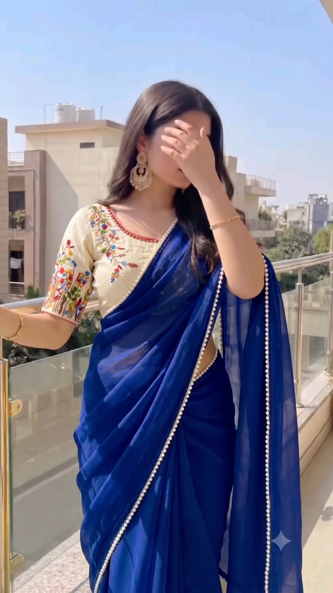 An off-white/cream cropped blouse with colorful floral embroidery on the sleeves and neckline, laid flat on a light beige background.